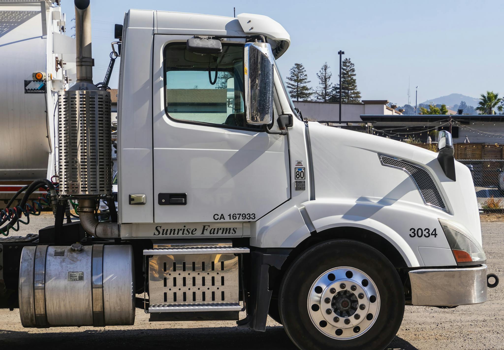 Side view of a white semi-trailer truck parked outdoors in an industrial area.